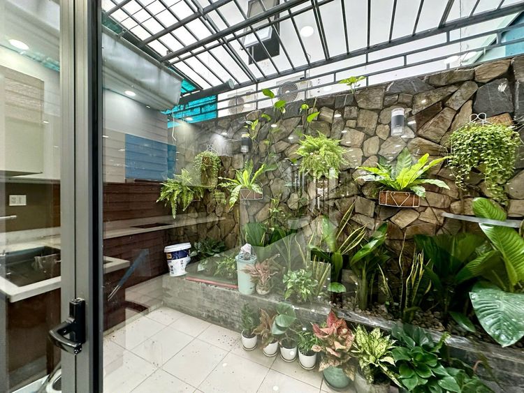 Giếng trời trong nhà phố Vạn Phúc City với mái kính khung sắt, tường ốp đá chẻ và nhiều chậu cây lá xanh, nhìn qua cửa kính từ trong nhà