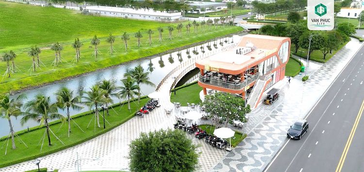 Tòa nhà Sugar Town màu cam đỏ bên kênh Sông Trăng, có cầu nhỏ, hàng dừa và vỉa hè lát đá hình sóng