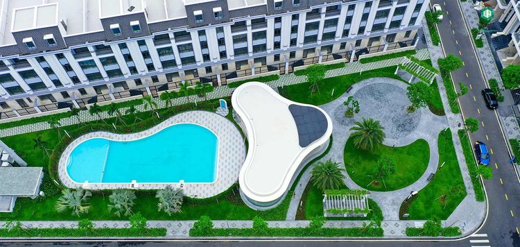 Hồ bơi xanh hình hạt đậu cạnh khối clubhouse mái cong trắng, bao quanh là thảm cỏ và dãy nhà phố