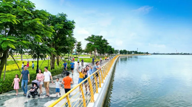 Gia đình và khách tham quan đi dạo trên lối đi bộ có lan can vàng sát mặt sông, bên cạnh hàng cây xanh