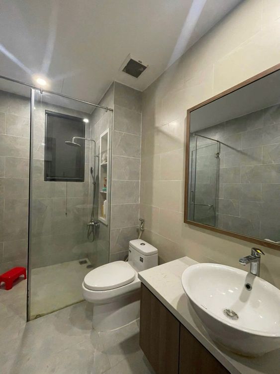 Phòng tắm nhà phố Vạn Phúc City với vách kính tắm đứng, tường ốp gạch xám, bồn rửa đặt trên tủ gỗ và gương khung gỗ lớn