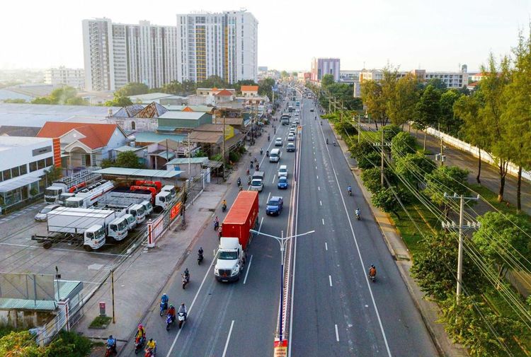Quốc lộ 13 hướng về phía Bình Dương cũ ngày khô ráo, xe tải và xe máy lưu thông, bên trái là bãi xe và nhà xưởng