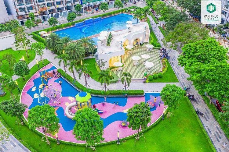 Sân chơi trẻ em nền cao su màu hồng và xanh dương cạnh hồ bơi và hàng cọ trong công viên khu Đông Nam