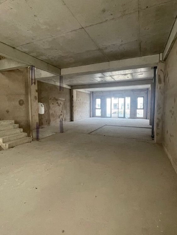 Bên trong căn nhà phố thô ở Vạn Phúc City: sàn và trần bê tông trơn, tường chưa hoàn thiện, cầu thang bê tông và cửa kính phía cuối