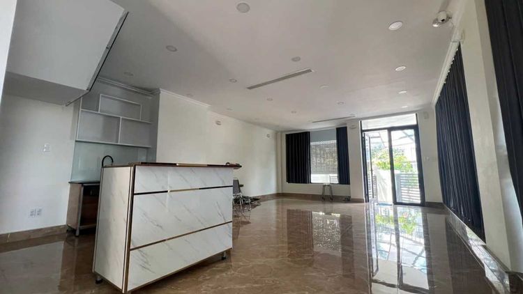 Tầng trệt trống lát đá bóng của căn góc 8x20 m cho thuê, có quầy bếp và cửa kính ra sân